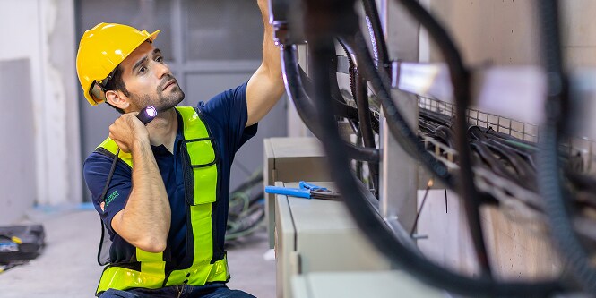 worker in safety gear inspecting electrical cable management with flashlight
