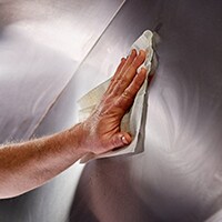 Close-up of a restaurant worker’s hand, cleaning a stainless-steel surface in a commercial kitchen.