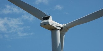 Photograph of a close-up view of a white wind turbine against a blue sky with scattered clouds.
