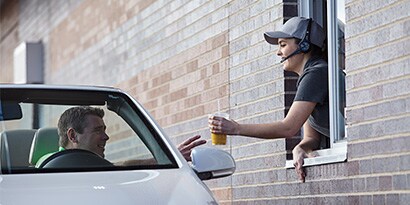 woman hands smoothie through a drive-thru window using 3M headset accessories