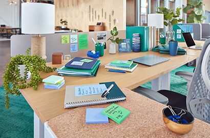 a desk covered in notebooks, desk accessories, and colorful Post-it® notes