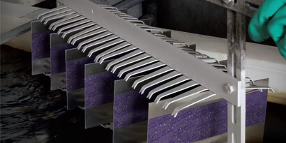 Masked metal plates on a rack as a worker is about to lower them into an anodizing solution.
