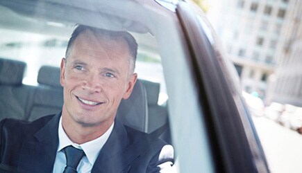 A professional man smiles as he comfortably drives without sunglasses on a sunny day.