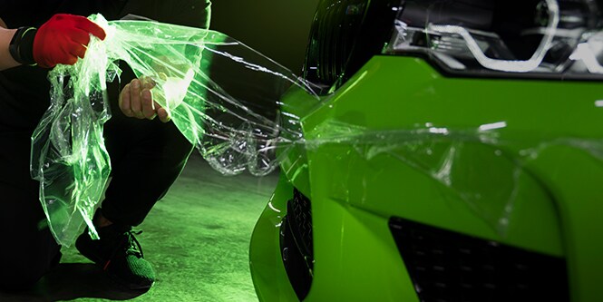 man with red glove applying wrap film to side of car

