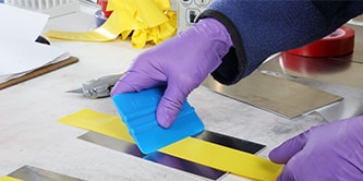 Gloved hands smooth out yellow tape on metal with 3M™ Hand Applicator PA1
