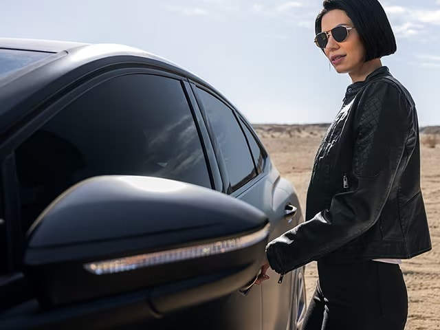 Woman grabbing door handle of black sedan with matte paint protection film in the desert