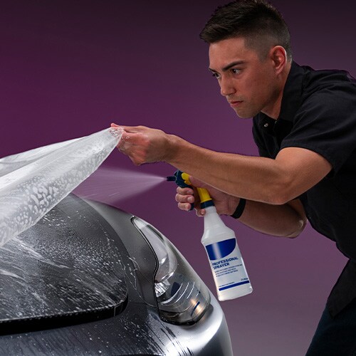 Man spraying water during paint protection installation on hood of car