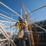 Image showing a construction worker wearing a safety harness and helmet, standing on scaffolding at a building site