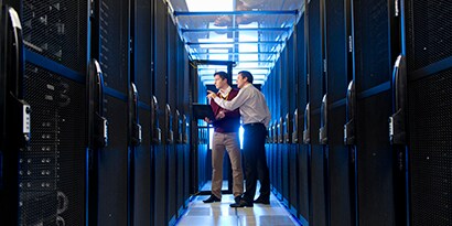 Two men standing among a row of servers trying to solve a problem.
