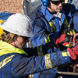 worker in coveralls wearing a hardhat and earplugs outside