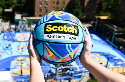 Person holding Scotch® branded basketball in front of colorful painted basketbal court