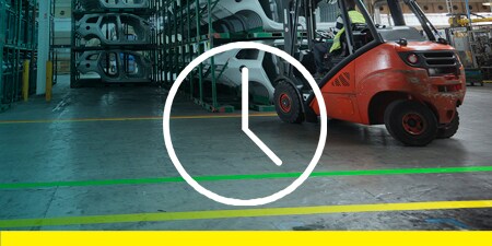 Image of a forklift on a taped off floor placing a vehicle frame on a rack; overlay of a clock icon representing efficiency
