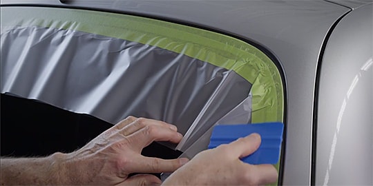 Video still with text “Wipe tape down with 3M Plastic Applicator PA-1” as being used on window edge
