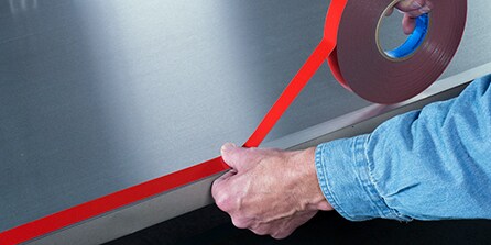 person attaching vhb tape to frame
