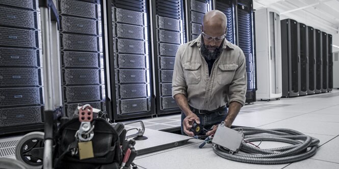 worker working on sub-floor electrical equipment maintenance in front of server racks
