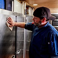 A restaurant worker cleans the surface of a commercial refrigerator.