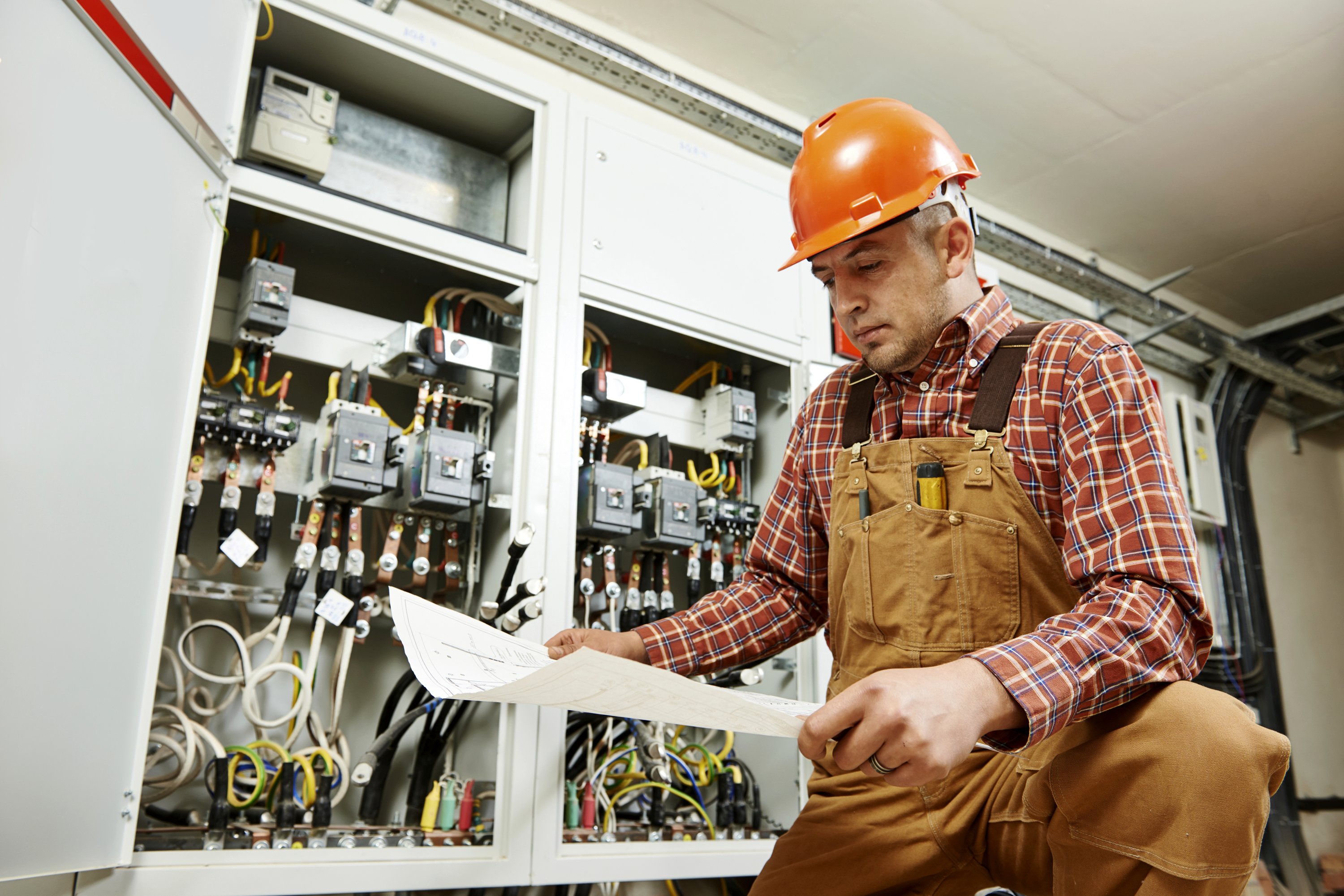 Electrician sitting in front of electric panel looking at blueprints
