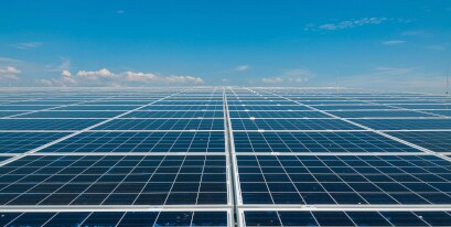 Solar panels in a grid on a flat plain, reaching to the visible horizon under a clear blue sky.
