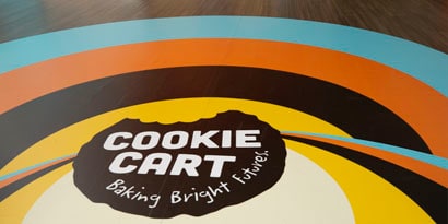 A floor graphic displays a colorful, circular branding design for 'Cookie Cart'.
