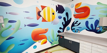 A wall has an interior graphics wrap with images of cheerful, brightly colored fish.
