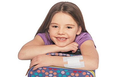 Girl hugging her backpack with Nexcare™ Gentle Paper Tape bandage on her arm.