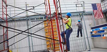 Worker in fall protection gear climbing ladder in fall protection training facility
