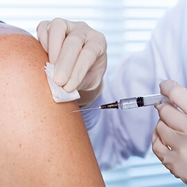 Clinician in white coat administers injection to patient